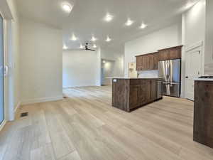 Kitchen with stainless steel appliances, backsplash, dark wood finish cabinets, light wood-type flooring, and open floor plan