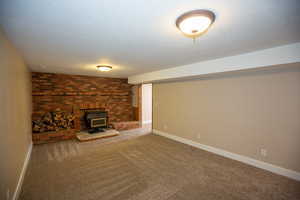 Unfurnished family room with carpet flooring, a wood stove, and a textured ceiling