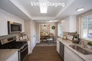 Virtually Staged Kitchen featuring stainless steel appliances, white cabinets, dark LVP floors, decorative light fixtures, and light stone counters