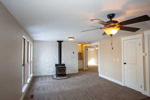 Unfurnished family room featuring a wood stove, carpet, and ceiling fan