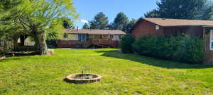 Expansive lawn featuring a brick fire pit, mature trees, and a rear deck with a ramp