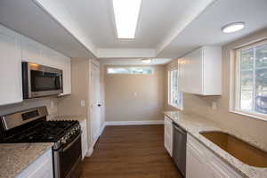 Updated kitchen with stainless steel appliances, white cabinets, dark LVP floors, light granite countertops, and a tray ceiling