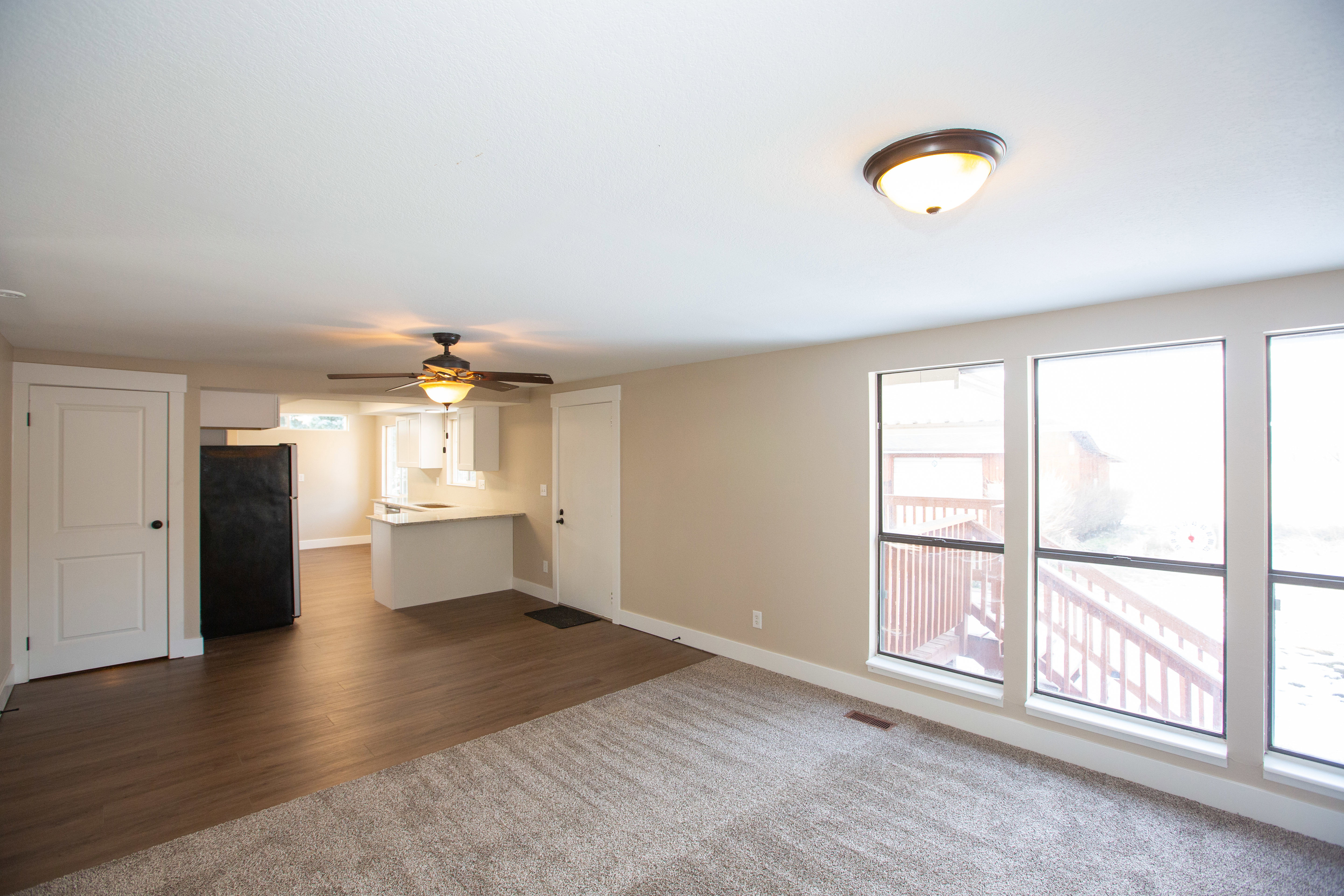 Unfurnished living room with ceiling fan, dark wood finished floors, healthy amount of natural light, and dark colored carpet
