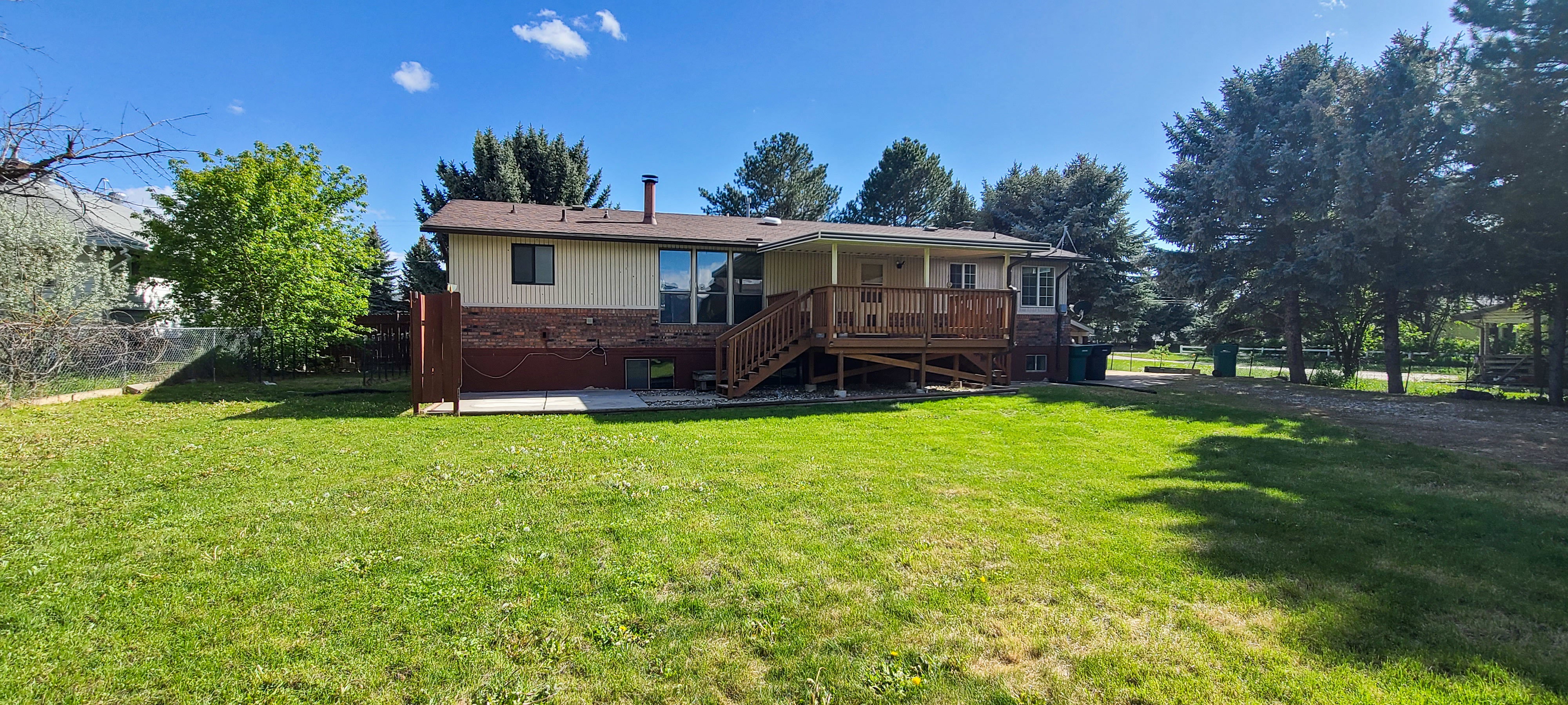 Expansive backyard featuring a manicured lawn, a covered wood deck, and a concrete patio