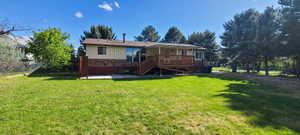 Expansive backyard featuring a manicured lawn, a covered wood deck, and a concrete patio