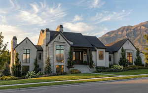 French country home featuring a chimney, stone siding, a front yard, and stucco siding