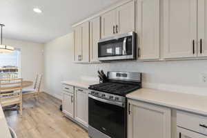 Kitchen featuring stainless steel appliances, backsplash, light wood finished floors, pendant lighting, and light stone countertops