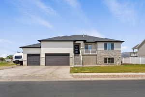 Prairie-style house with stone siding, an attached garage, driveway, and a shingled roof