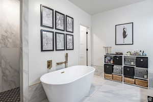 Bathroom featuring a freestanding bath, marble look tile flooring, a wainscoted wall, and a marble finish shower