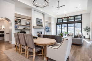 Dining area with hanging lights, light wood-style floors, ceiling fan, a glass covered fireplace, and arched walkways