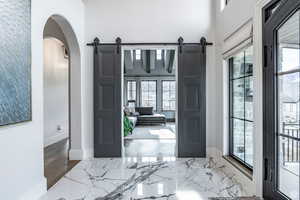 Foyer with a barn door, marble tiled floors, a high ceiling, and arched walkways