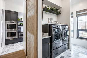 Laundry area with light marble finish flooring, washer and dryer, cabinet space, and a barn door