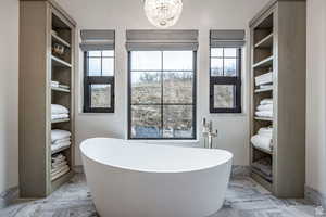 Full bath featuring marble tiled flooring, suspended lighting, a freestanding tub, and healthy amount of natural light