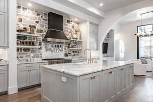 Kitchen with gray cabinetry, light stone countertops, decorative backsplash, open shelves, and open floor plan