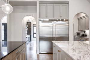 Kitchen featuring arched walkways, dark stone counters, stainless steel appliances, gray cabinets, and light wood-type flooring