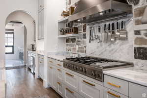 Kitchen with open shelves, stainless steel gas stovetop, light stone counters, exhaust hood, and dark wood-style flooring
