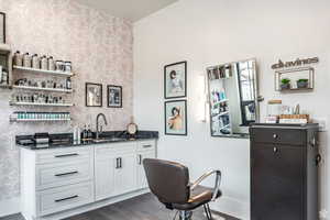 Indoor wet bar with open shelves, dark stone countertops, white cabinets, dark wood-type flooring, and wallpapered walls