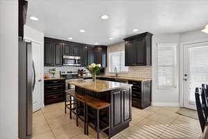 Kitchen with a kitchen breakfast bar, stainless steel appliances, light tile patterned floors, light stone counters, and recessed lighting