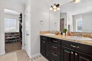 Full bathroom featuring a walk in closet, double vanity, and light tile patterned flooring