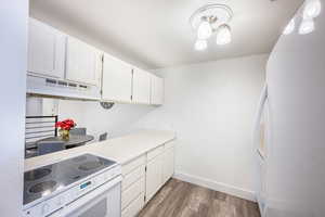 Kitchen with white appliances, white cabinets, light countertops, and dark wood-style floors