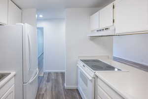 Kitchen with white cabinets, white appliances, light countertops, dark wood-style floors, and recessed lighting