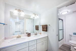 Full bathroom with double vanity, bath / shower combo with glass door, and dark wood-style flooring