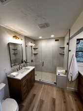 Full bathroom with vanity, light wood-style flooring, a shower stall, and a textured ceiling