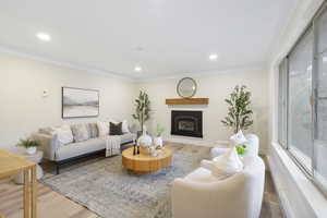 Living area featuring a glass covered fireplace, wood finished floors, crown molding, and recessed lighting