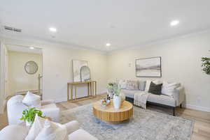 Living room with light wood-type flooring, ornamental molding, baseboard heating, and recessed lighting