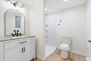 Bathroom featuring vanity, walk in shower, light wood finished floors, and recessed lighting