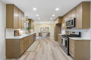 Kitchen with backsplash, stainless steel appliances, light wood-type flooring, light stone counters, and a chandelier