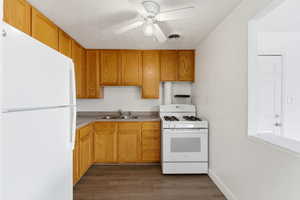Kitchen with white appliances, ceiling fan, dark wood finished floors, light countertops, and wood finish cabinets