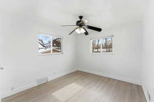 Empty room with ceiling fan, light wood-style flooring, and plenty of natural light
