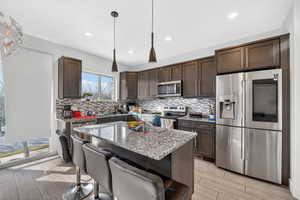 Kitchen featuring stainless steel appliances, a kitchen breakfast bar, dark wood finish cabinets, light stone counters, and wood finish floors
