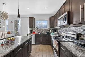 Kitchen with stainless steel appliances, dark wood finish cabinets, light stone countertops, light wood-style floors, and pendant lighting