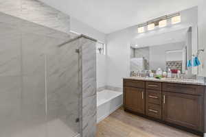 Full bathroom with double vanity, a bath, light wood-type flooring, and a marble finish shower