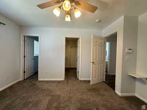 Unfurnished bedroom featuring a walk in closet, dark carpet, ceiling fan, and a textured ceiling