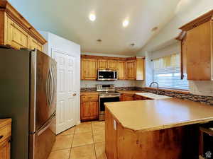 Kitchen with stainless steel appliances, a peninsula, light countertops, light tile patterned flooring, and lofted ceiling