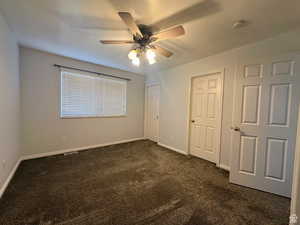 Unfurnished bedroom with dark carpet and ceiling fan