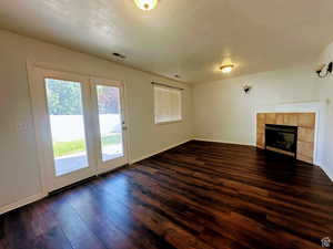 Unfurnished living room with dark wood-style floors and a tile fireplace