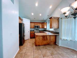 Kitchen with a peninsula, stainless steel appliances, lofted ceiling, light tile patterned floors, and wood finish cabinets