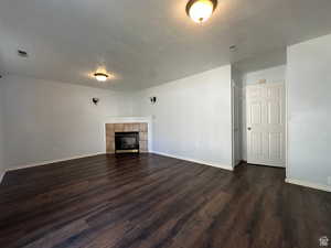 Unfurnished living room with a tiled fireplace, dark wood-style floors, and a textured ceiling