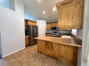 Kitchen featuring a peninsula, stainless steel appliances, light tile patterned floors, wood finish cabinets, and recessed lighting