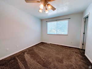 Unfurnished bedroom featuring dark colored carpet, a ceiling fan, and a textured ceiling
