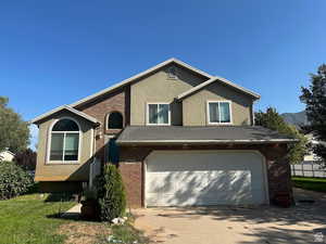 View of front facade featuring driveway, brick siding, and stucco siding