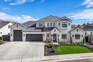 View of front of house with board and batten siding, stone siding, a front yard, concrete driveway, and a garage