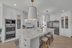 Kitchen featuring white cabinetry, parquet floors, built in appliances, and light stone counters