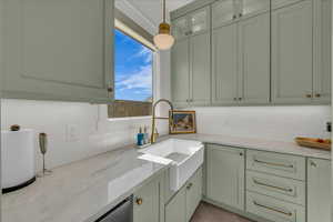 Kitchen featuring green cabinetry, light stone counters, hanging light fixtures, and decorative backsplash