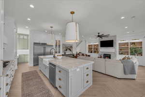 Two tone kitchen featuring hanging light fixtures, a kitchen island with sink, stainless steel appliances, parquet floors, and open floor plan