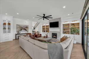 Living area featuring ceiling fan, built in shelves, a stone fireplace, parquet floors, and recessed lighting